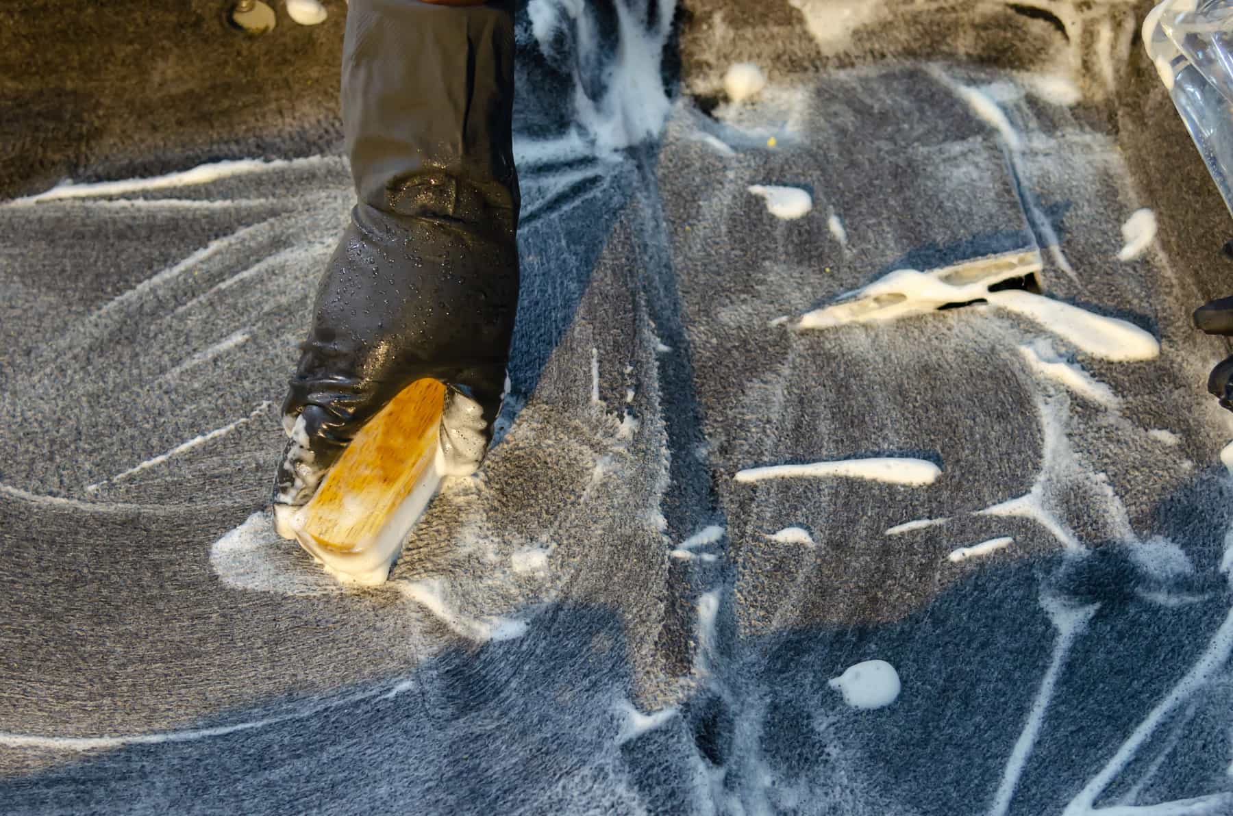 A rug being cleaned with a brush and cloth on a hard floor